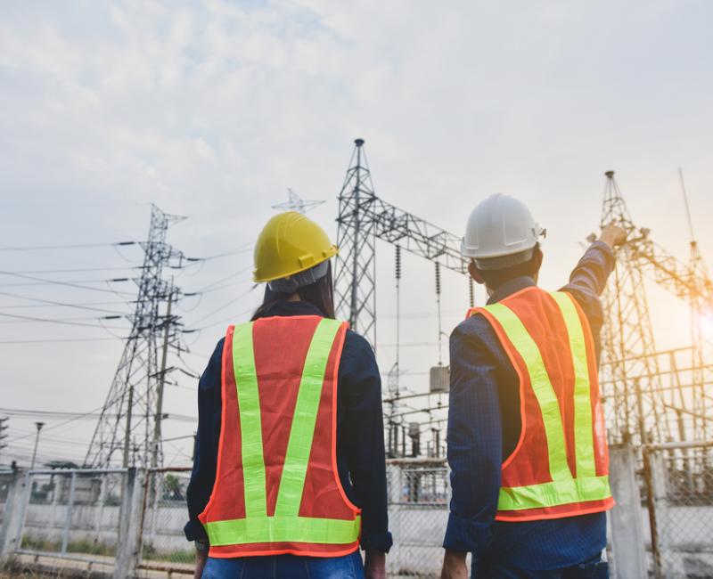 Two people cooperating in front of electricity transmission lines